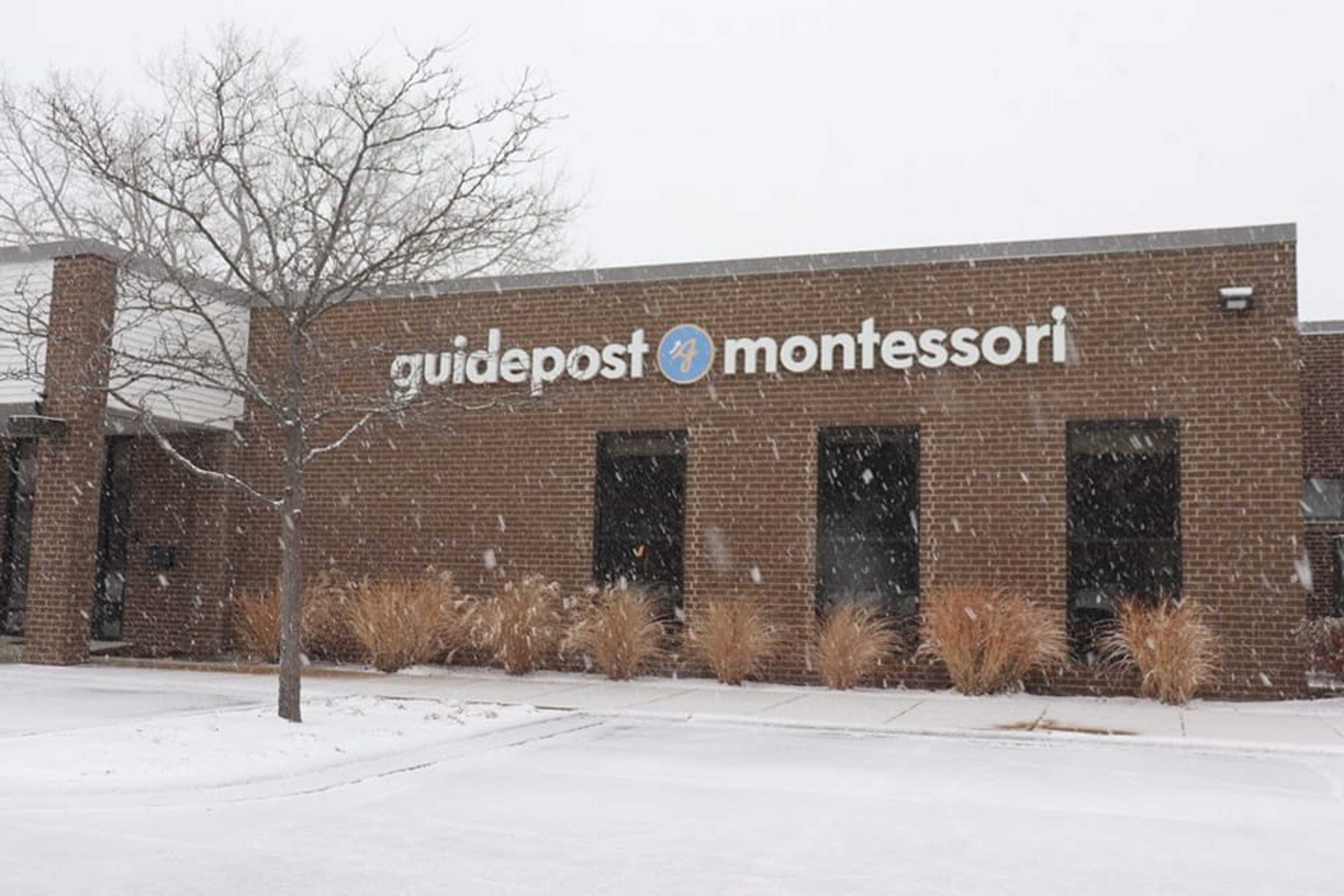 Close-Up view of Guidepost Montessori at Schaumburg that shows the brick exterior and 3 exterior windows as well as a branded Guidepost Montessori sign. Blue skies loom in the background.