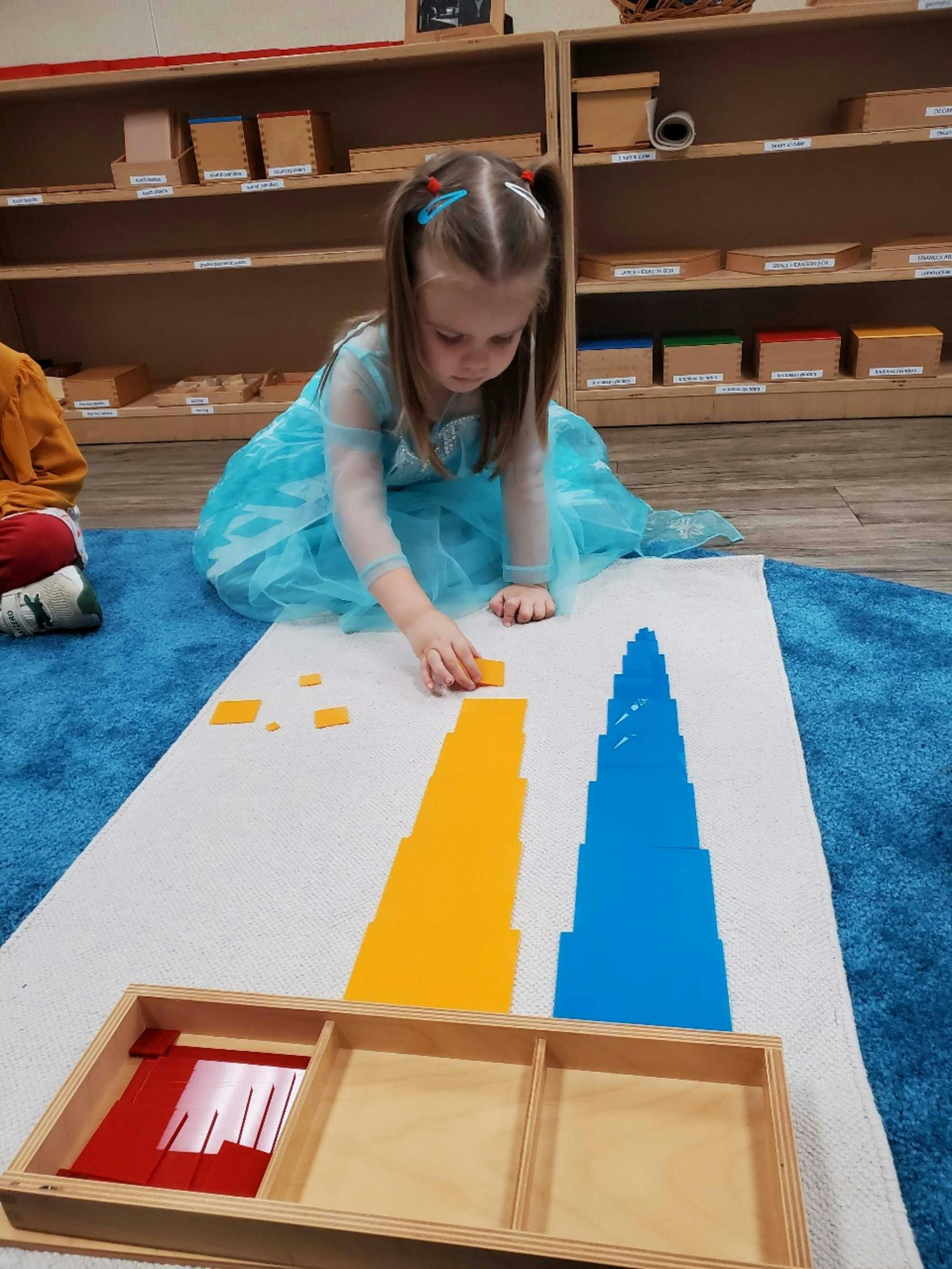 Children in a well-organized mixed-age Montessori classroom ponder over an activity using blocks of different sizes, classic Montessori classroom materials
